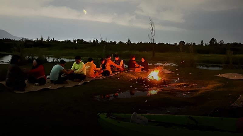 Personas reunidas junto al fuego a la orilla del canal al caer la noche